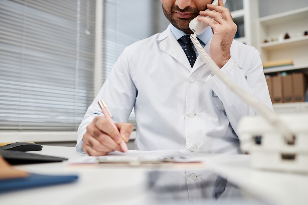 Physician on a desk phone while writing notes