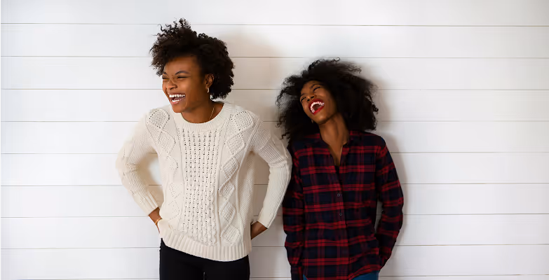 Two women laughing in front of a white wall, symbolising diversity, inclusion, and employee engagement at HR DataHub.