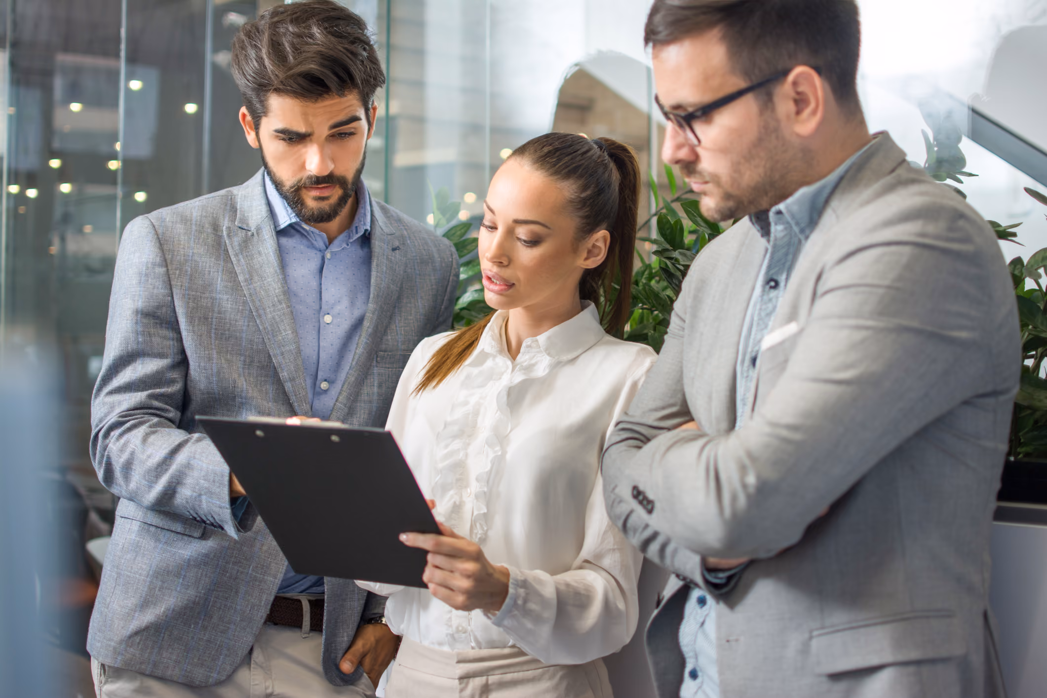 Three business professionals reviewing documents on a clipboard in an office setting.