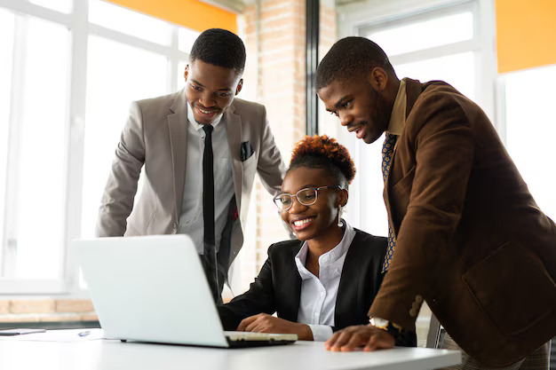 Three colleagues in business attire gathered around a laptop, discussing a project together in an office