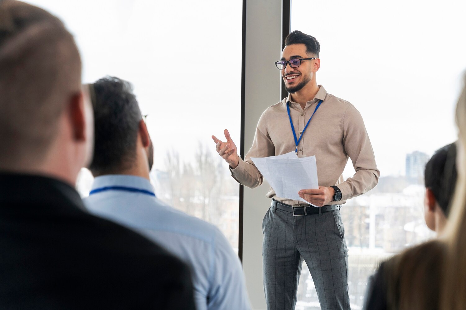 A man giving a presentation to a seated audience, gesturing while holding notes