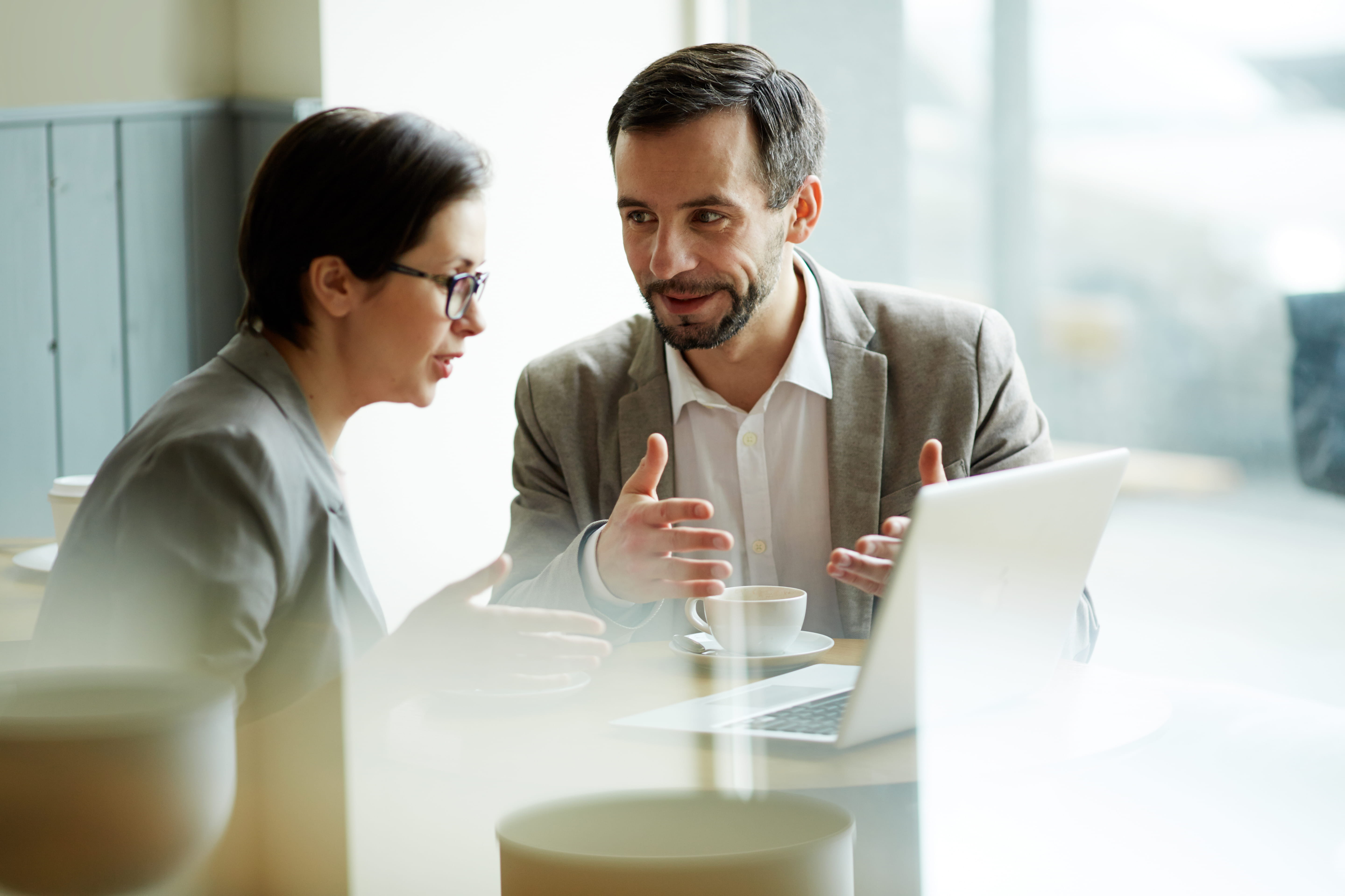 A man and woman having a conversation at a table with a laptop and coffee
