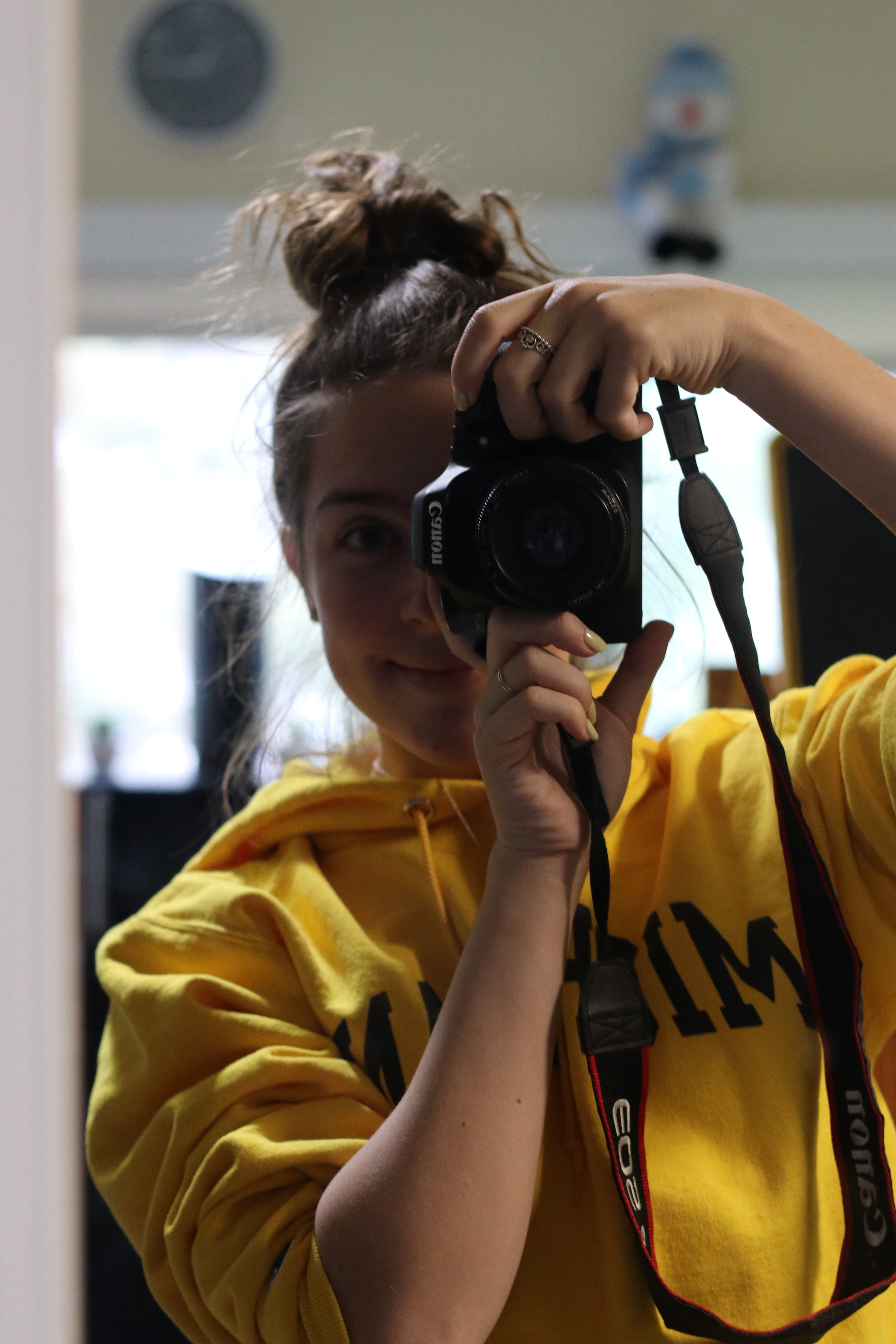 Sarah in yellow sweatshirt holding up camera in mirror