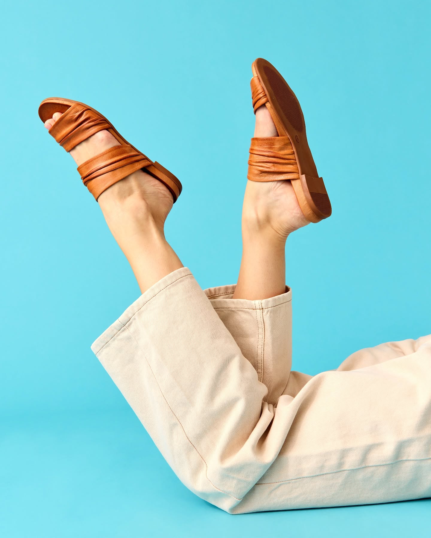 Tan leather Miz Mooz slide sandals on a blue background