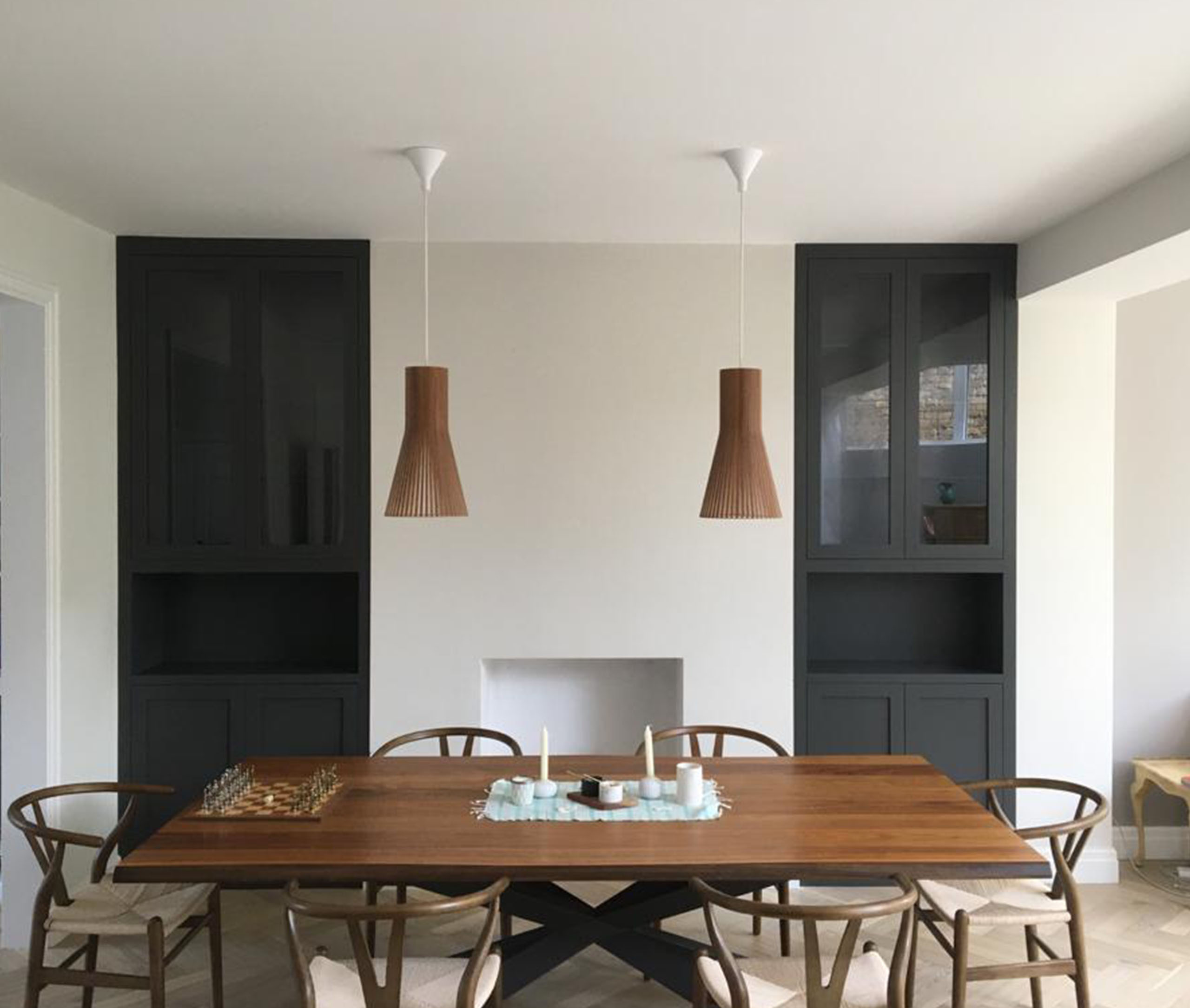 Modern dining room with a wooden table, six chairs, two pendant lights, and built-in black cabinets.