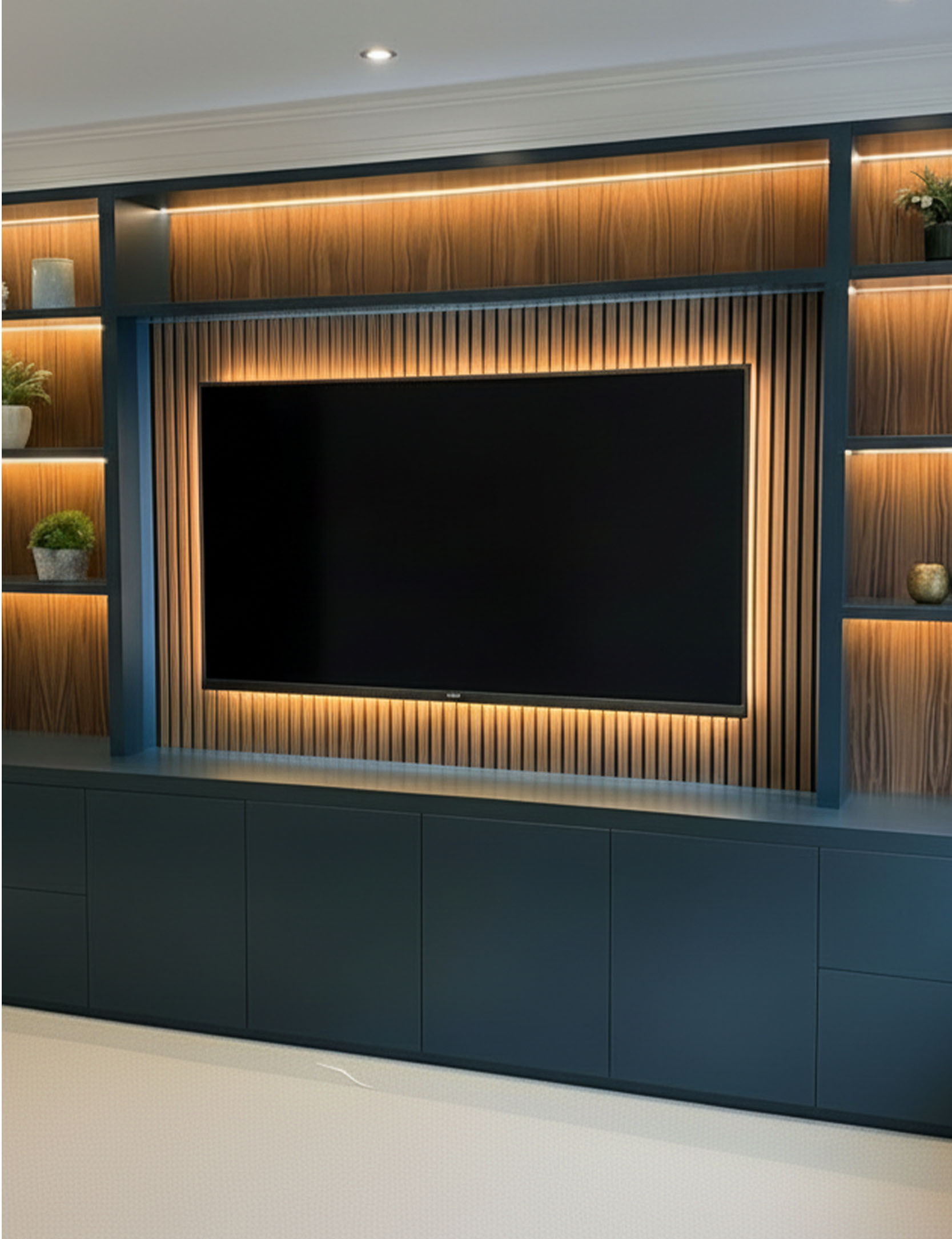 Wall-mounted flat-screen TV with a wooden slat backdrop and warm LED lighting, surrounded by blue shelving units with decorative plants and objects.