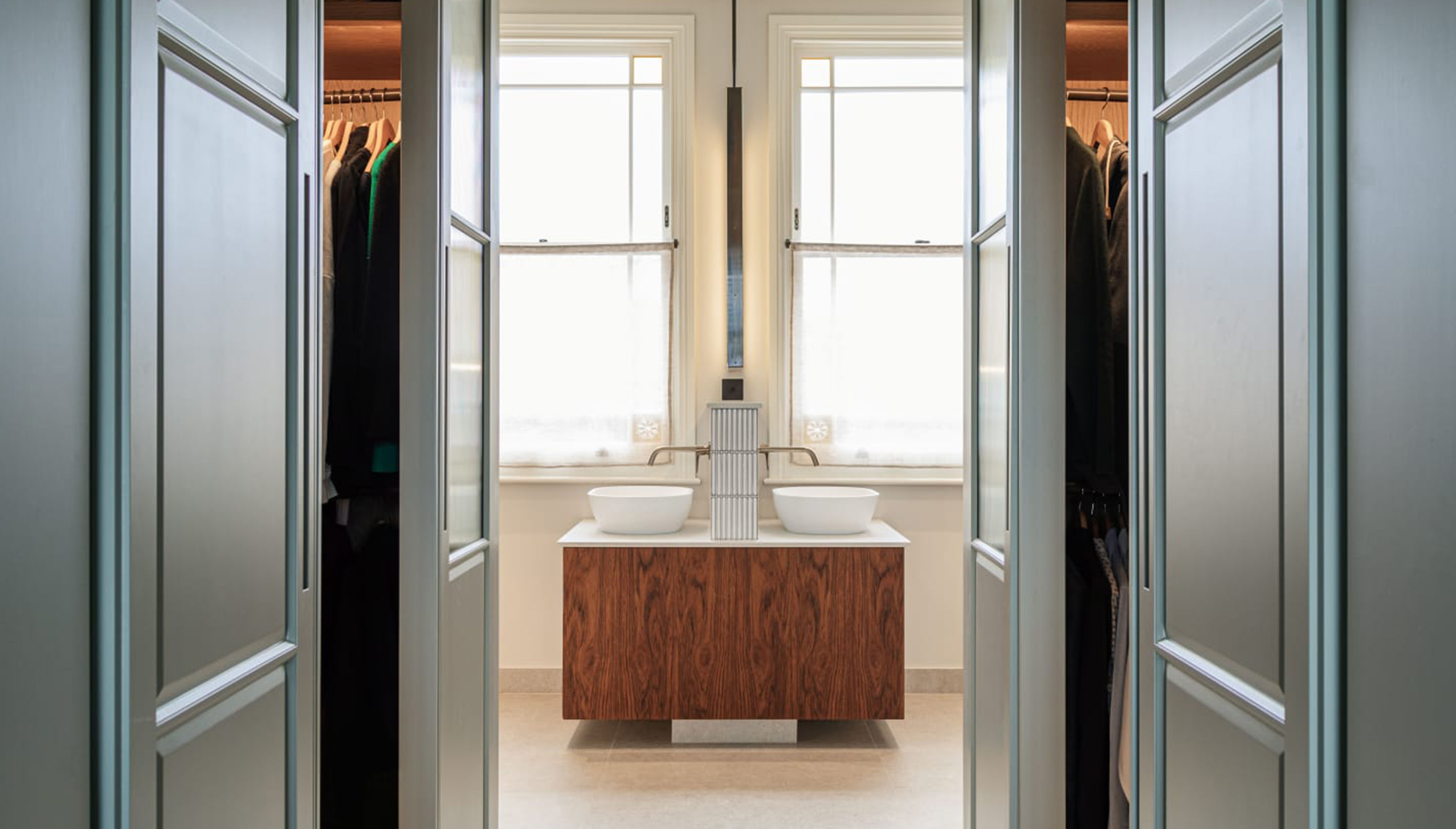 Beige three-drawer dresser with brass knobs and a white marble top, placed in a room with double doors and a window in the background.