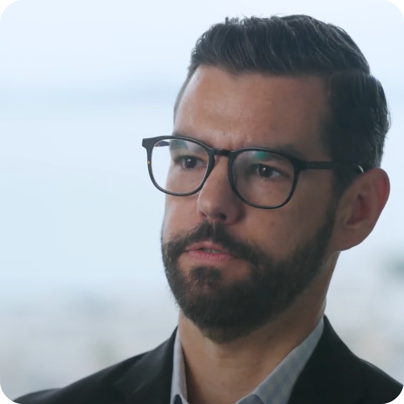 Man with short dark hair wearing a gray suit jacket and white shirt smiling against a beige background.