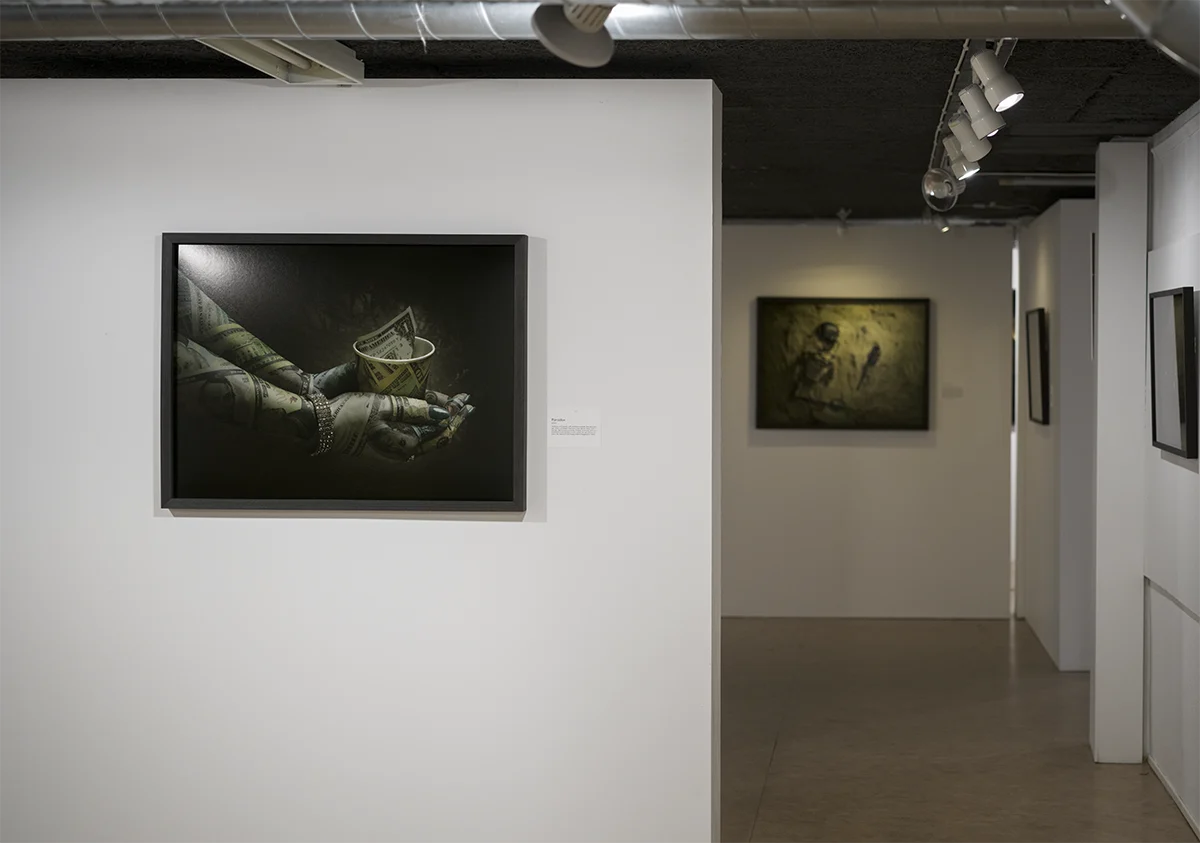 Ljus utställningshall med ett konstverk med en hand som håller en kopp och ett annat konstverk längre bakom på en annan vägg.