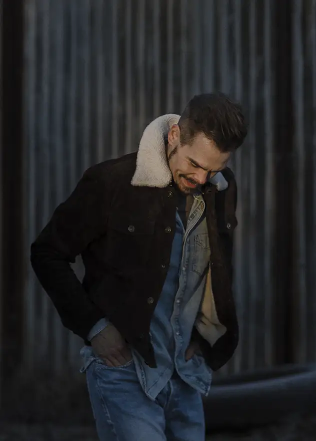 Artist standing in front of a steel wall, looking down, in background you can see his silhouette and shadow on the wall. 