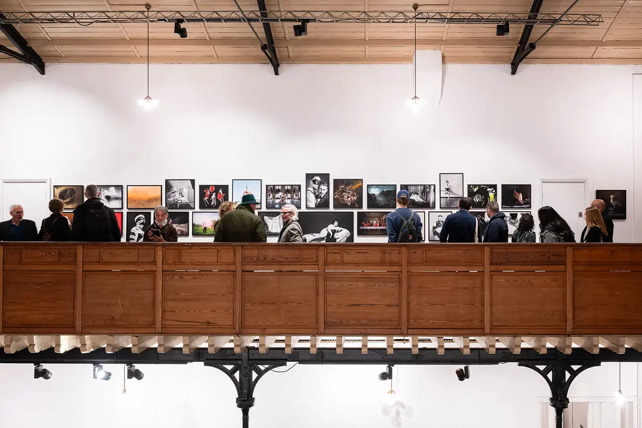 Utställning med många besökare som tittar på mindre konstverk arrangerade på en vit vägg.