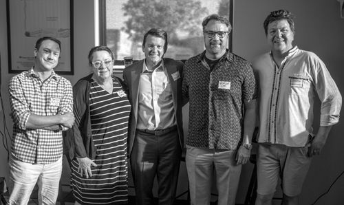 Group of five adults standing indoors, smiling and posing for a photo with name tags visible on their chests.
