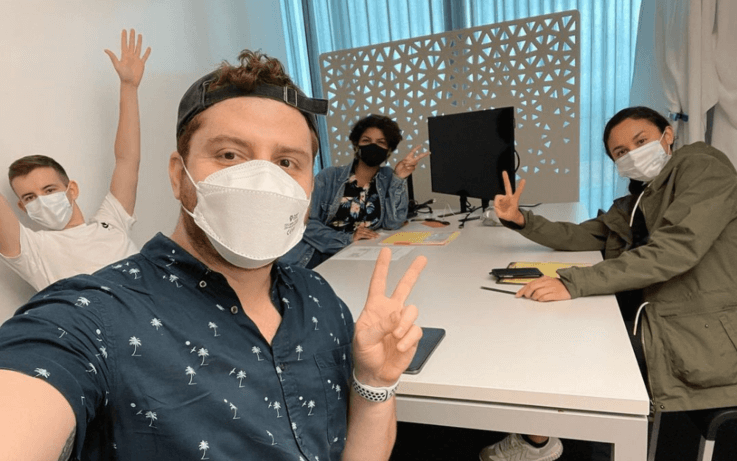 four sitting at white desk with face masks on and computer