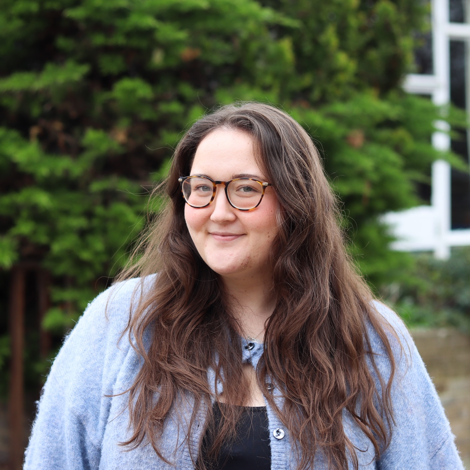 Image of a white woman, from the chest up, with brown hair and glasses.