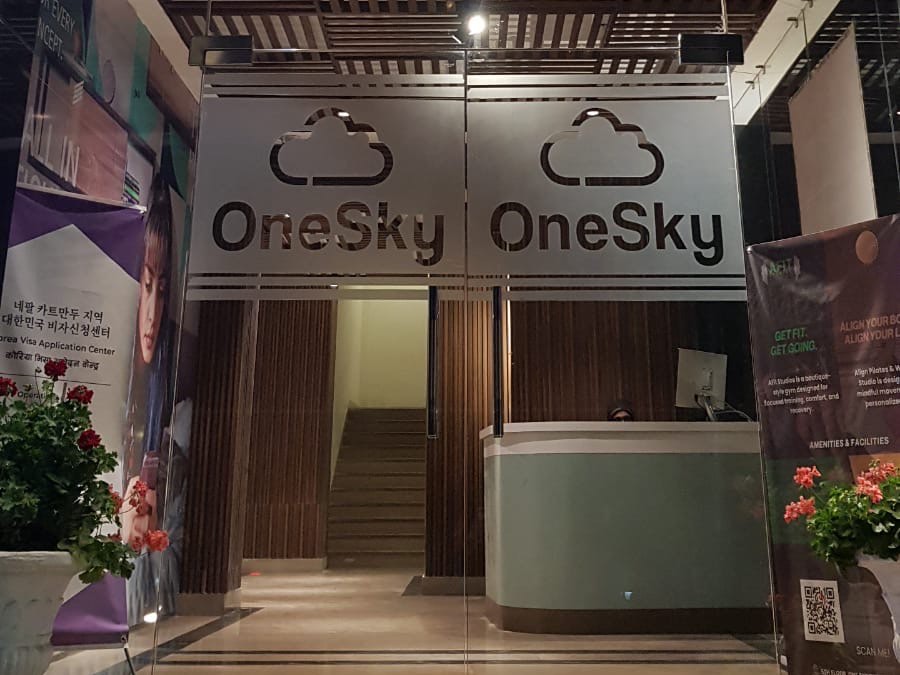 The lit OneSky entrance at street level, with glass doors and reception beyond