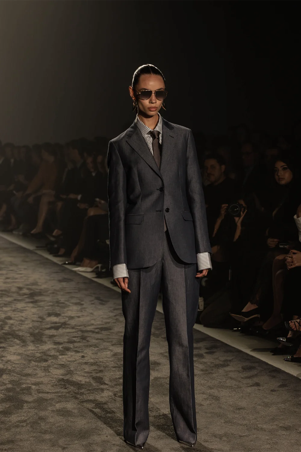 Model in a tailored charcoal suit with sunglasses and striped shirt on the Farage Australia Summer 26 runway at AFW 2025.