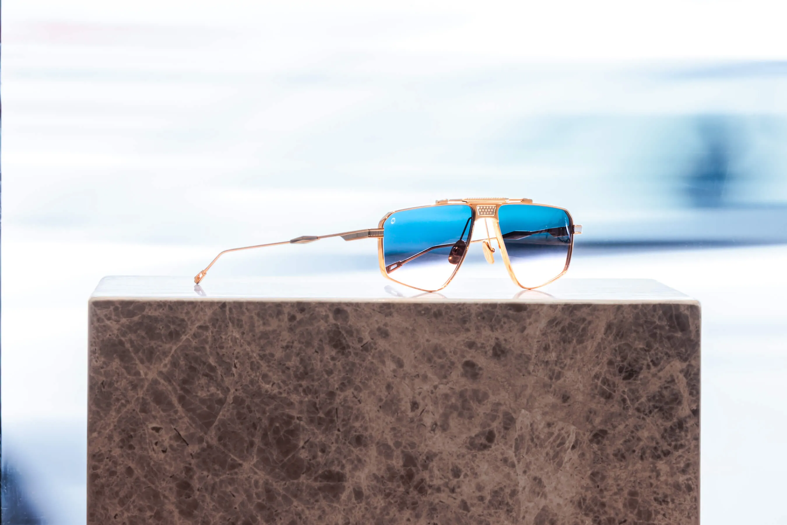 Showcase image of gold-frame aviator sunglasses with reflective blue lenses, styled atop a marble pedestal. The mirrored surface and crisp lines convey modern luxury and technical precision | EDG Studios