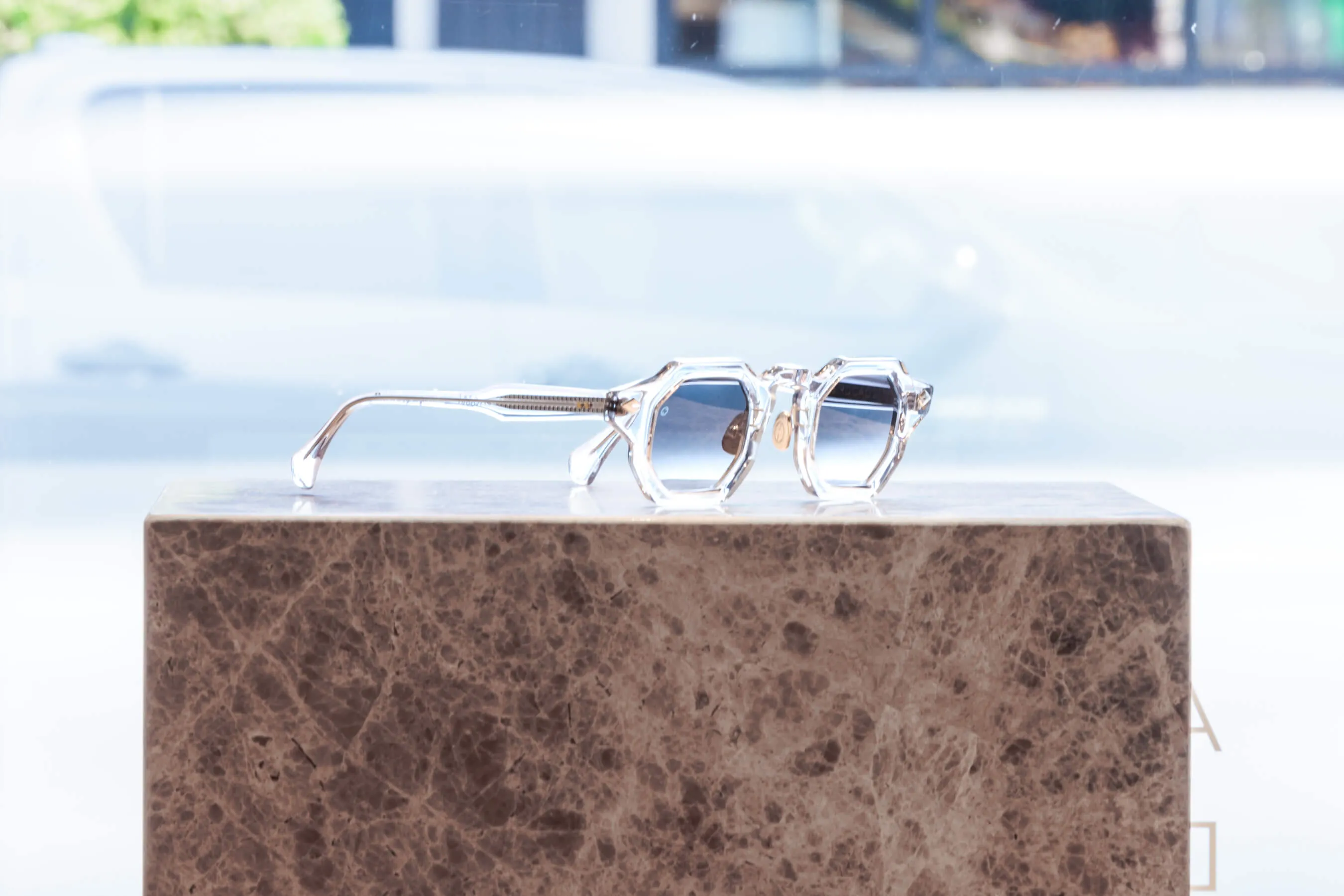 Brighter exposure of the clear hexagonal sunglasses against a sunlit window. Reflections and lens detail are more pronounced, underscoring the avant-garde aesthetic of the frame design | EDG Studios