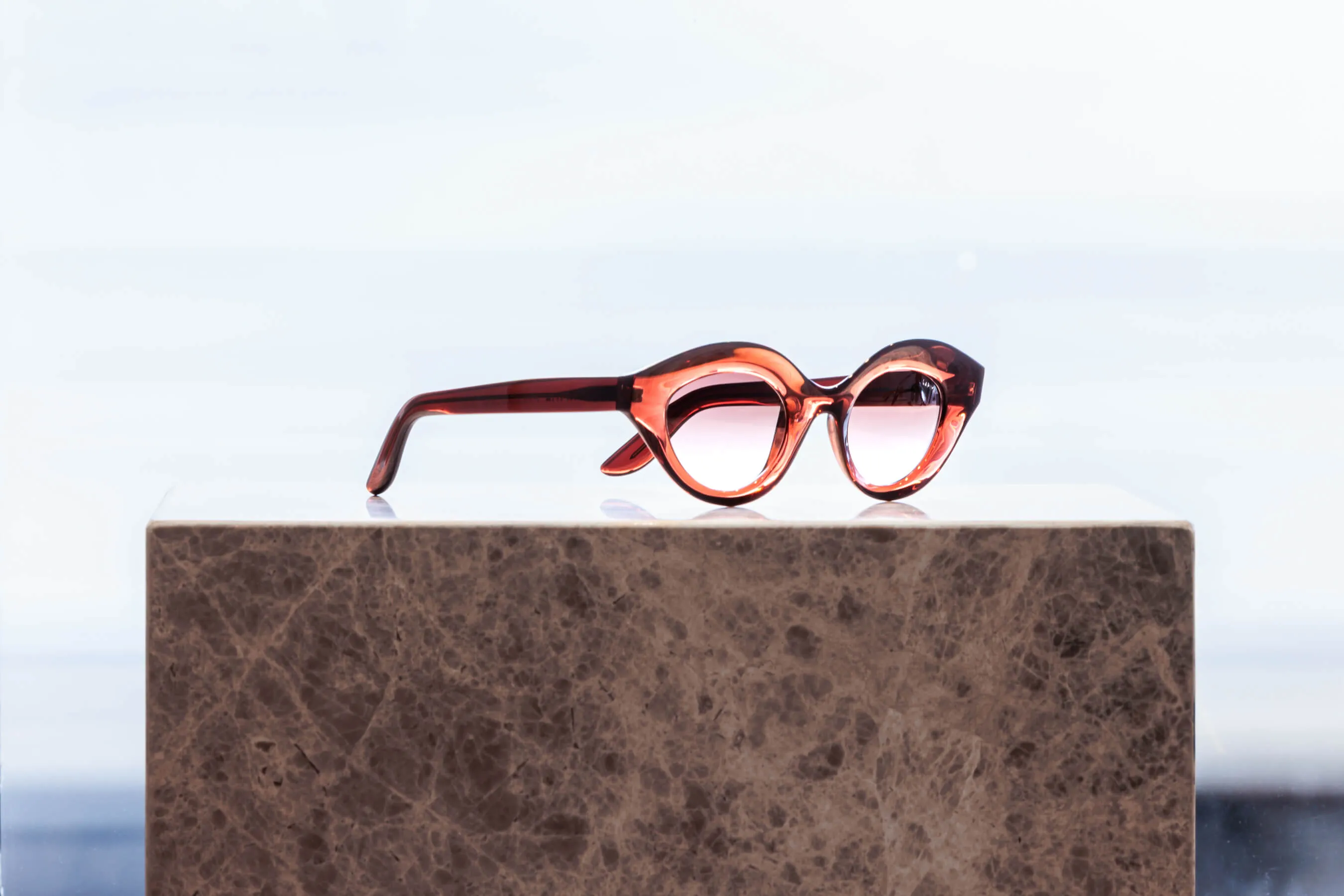 Red designer sunglasses with pink gradient lenses displayed on marble stand at Essu | EDG Studios