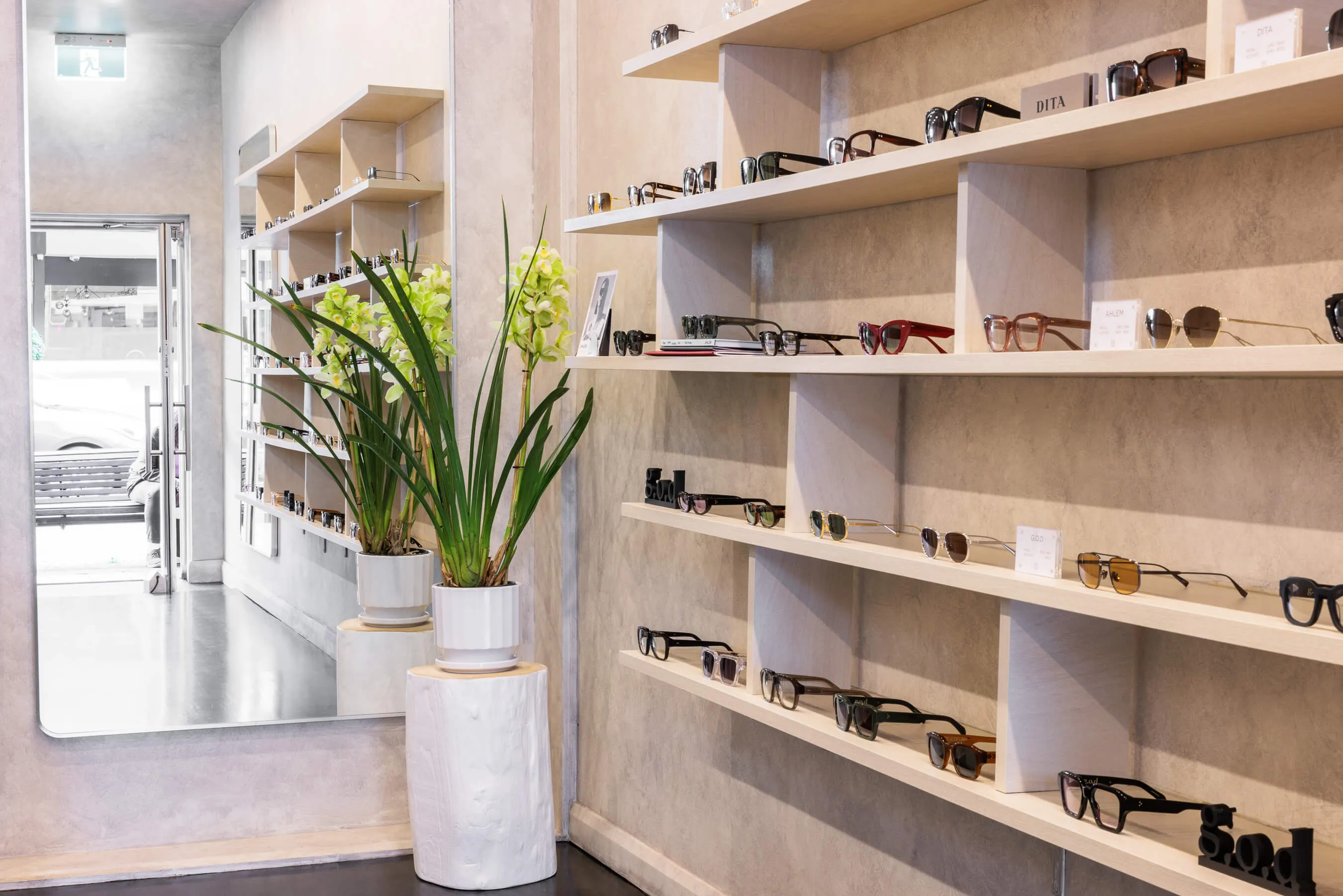 Interior of Essu Eyewear store with glasses on shelves, a large mirror, and potted plants in the entryway | EDG Studios