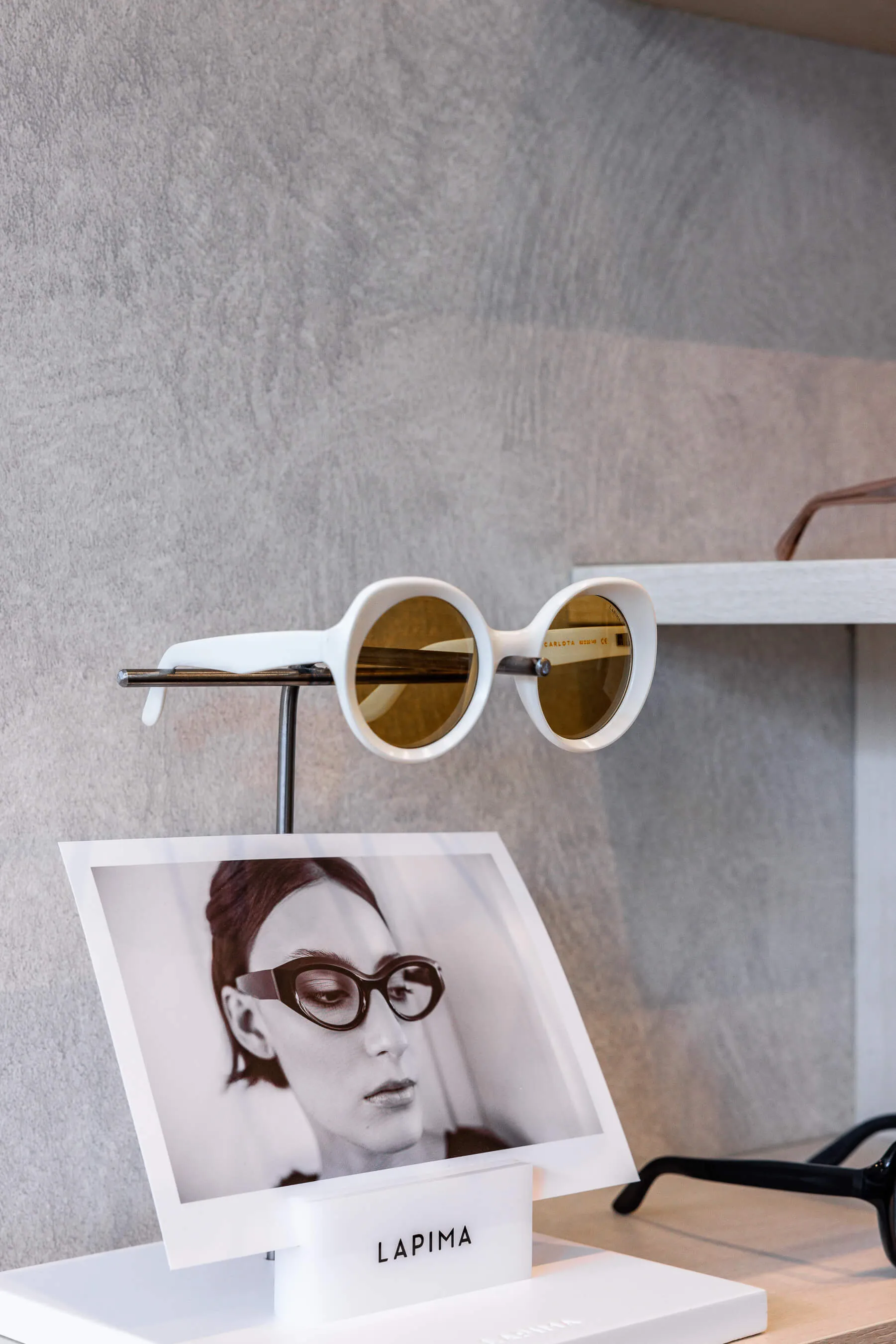 Essu Eyewear Image 14 Product and branding detail of LAPIMA’s white-framed round sunglasses, mounted above a promotional portrait of a model wearing the same design. Clean, editorial-style composition | EDG Studios