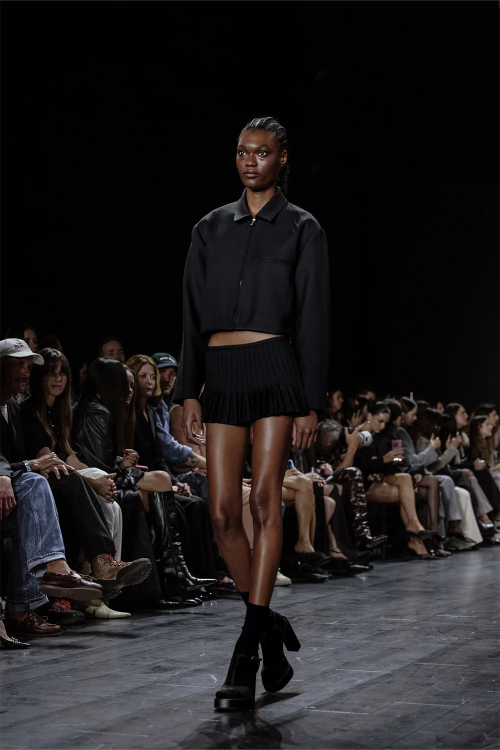 Model walks the Beare Park runway at Australian Fashion Week 2025 wearing a structured black cropped jacket and pleated micro skirt.