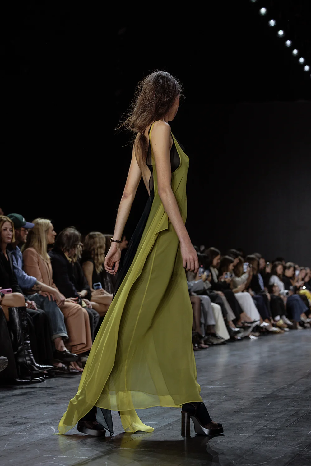 Side view of model in flowing olive green sheer gown with deep cutout back, walking the Beare Park runway at Australian Fashion Week 2025.