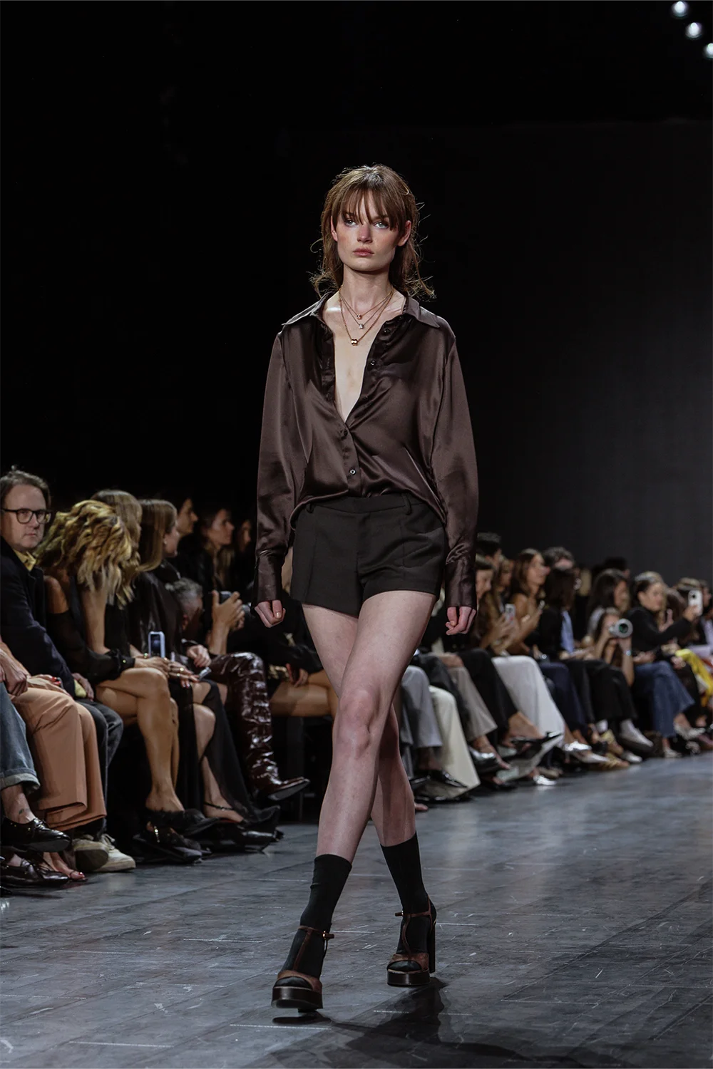 Beare Park runway look featuring a model in a chocolate satin blouse with deep neckline paired with tailored black shorts at AFW 2025.
