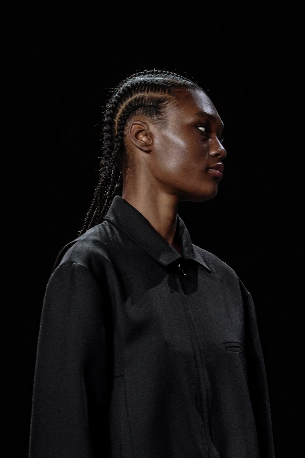 Profile close-up of model with braided hair wearing a black zip-up jacket, captured at Beare Park’s AFW 2025 runway show.