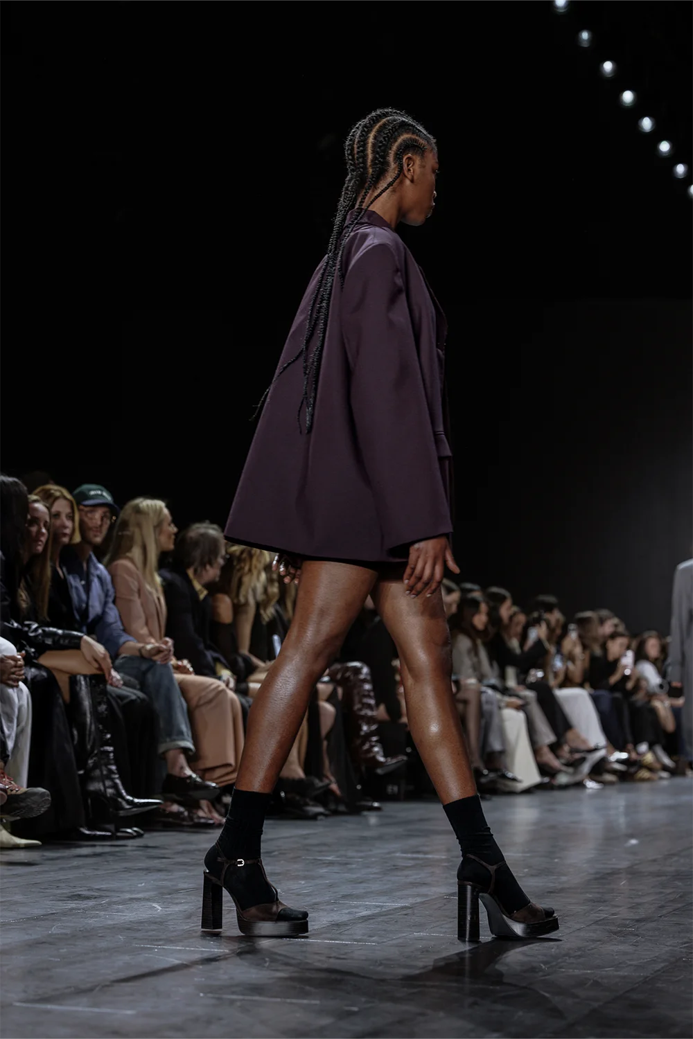 Side view of model in a plum blazer and mini set with cornrow braids at Beare Park, Australian Fashion Week 2025.