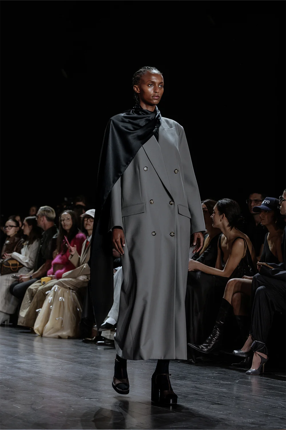 Model walks the Beare Park runway in a double-breasted grey coat with a dramatic black satin shoulder drape at AFW 2025.