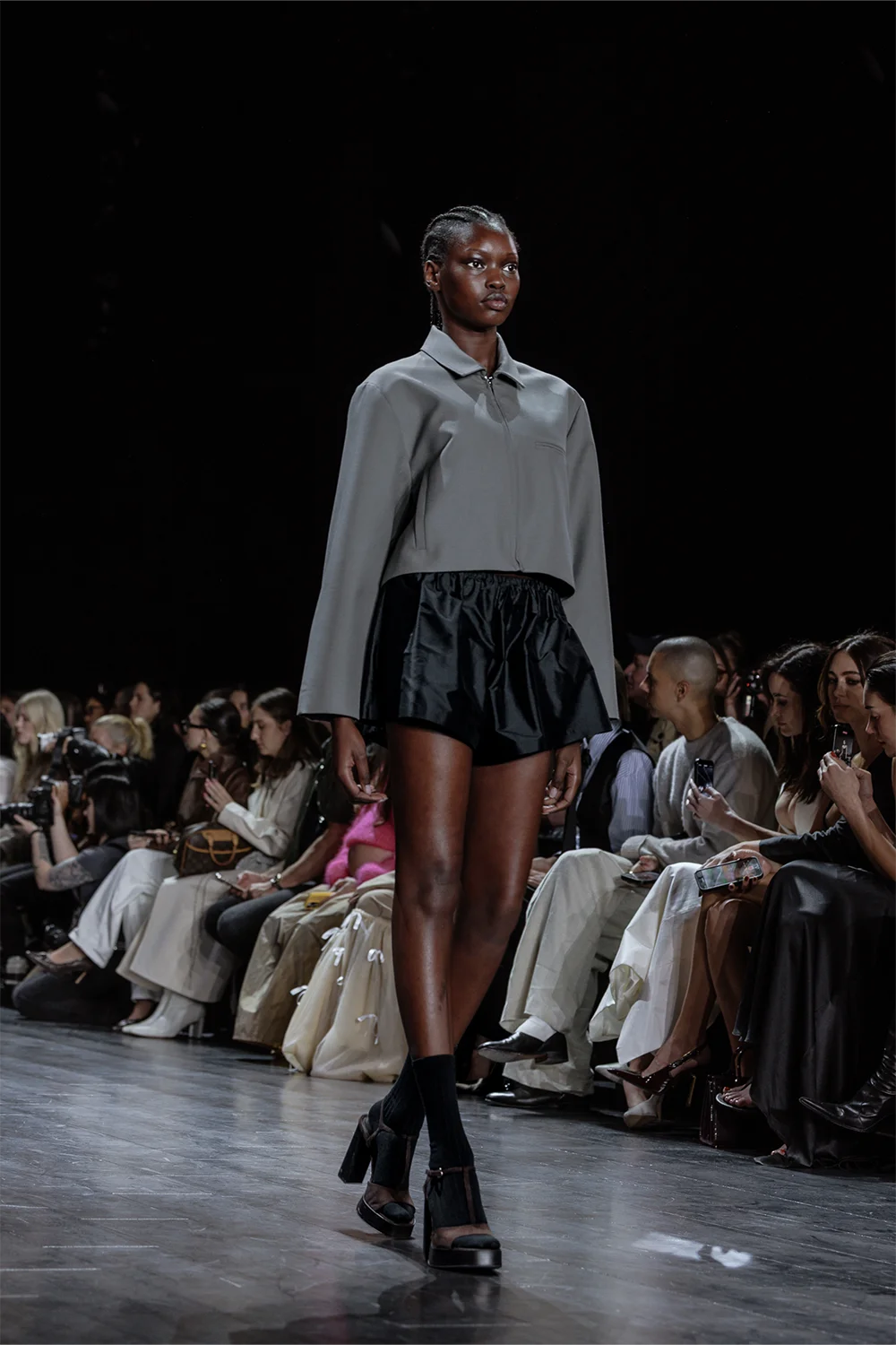 Model wears a cropped grey jacket with voluminous black satin shorts at Beare Park’s AFW 2025 runway presentation.