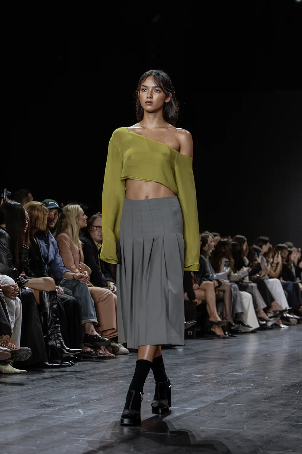 Runway look featuring a one-shoulder lime green chiffon crop top paired with a pleated grey high-waisted midi skirt and black heels.