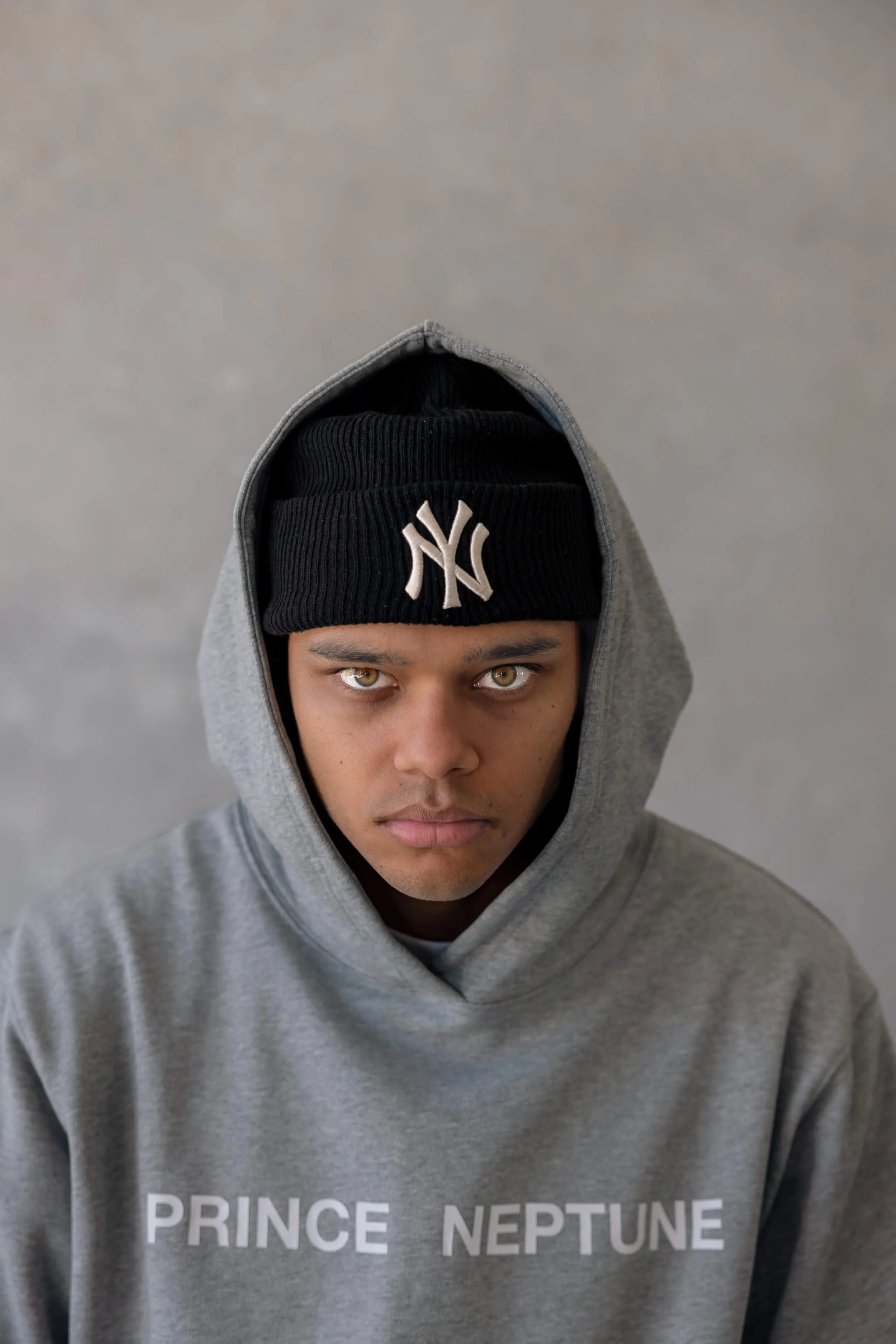 Close-up of model in hoodie and black beanie — Intense close-up portrait of a model wearing a black New York Yankees beanie and grey Prince Neptune hoodie, from the 2023 streetwear shoot | EDG Studios