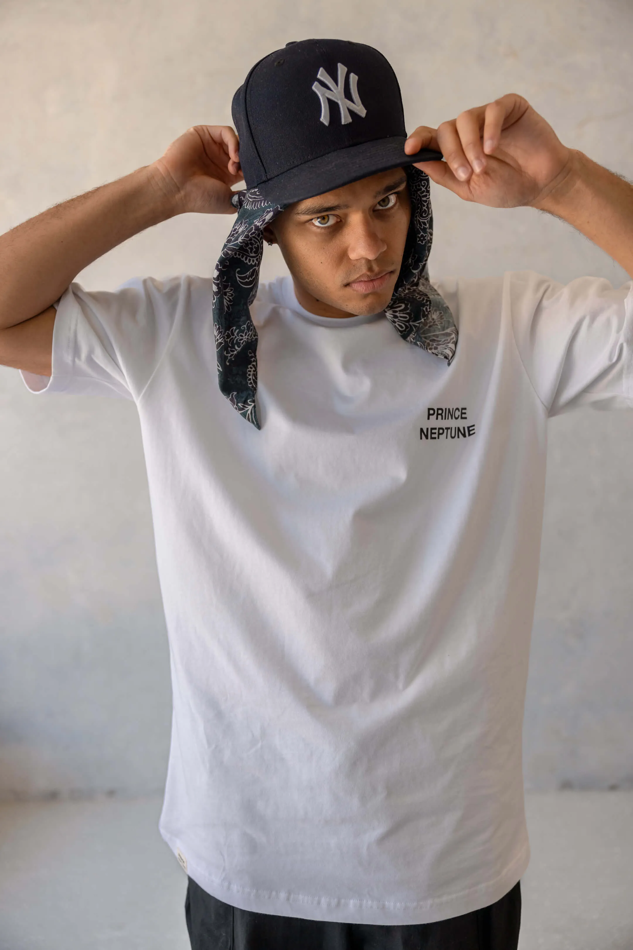 Model adjusting black Yankees cap with paisley bandana underneath, wearing Prince Neptune white T-shirt | EDG Studios