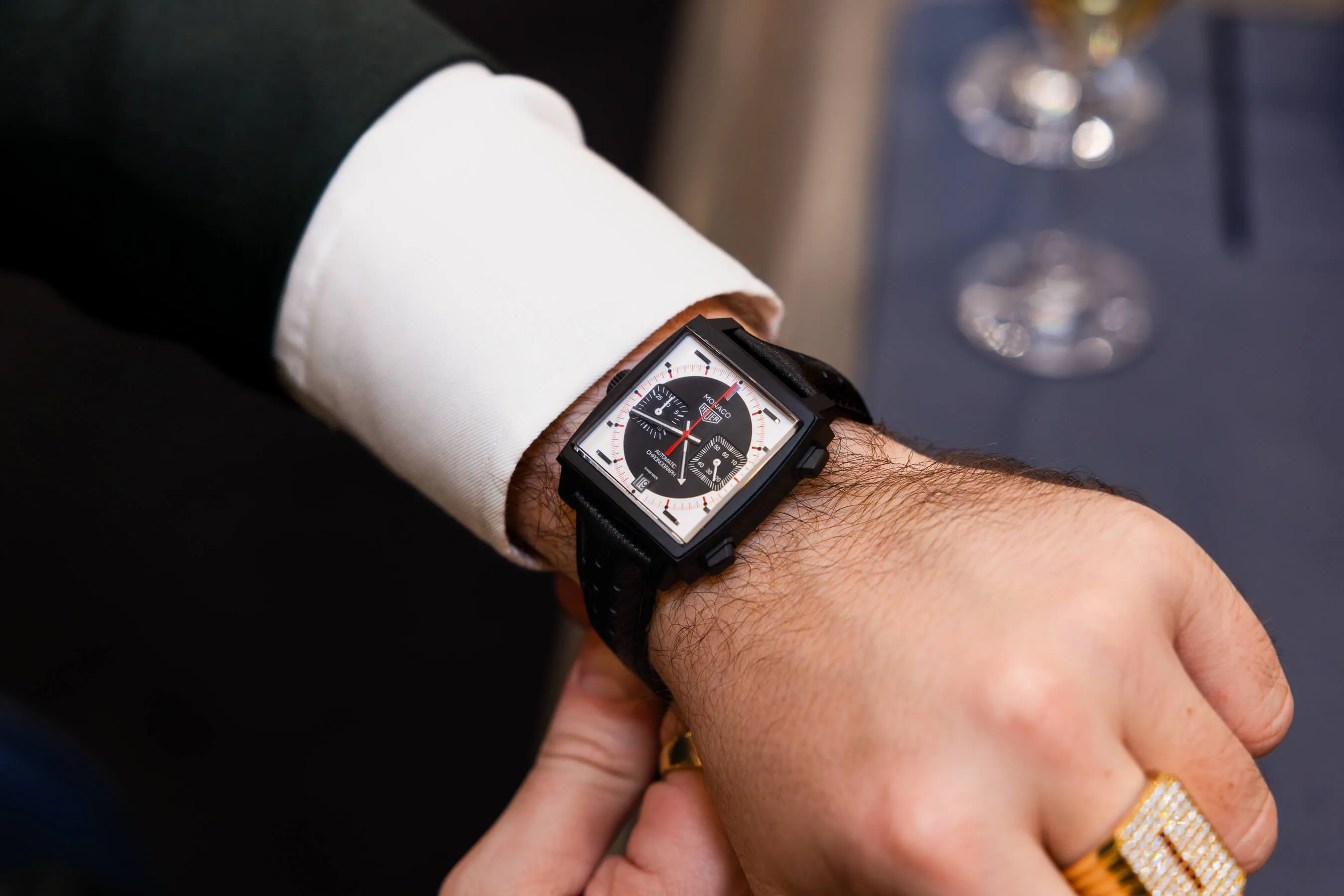 Close-up of a luxury TAG Heuer Monaco watch with a square black case, worn over a white dress shirt and green blazer sleeve | EDG Studios