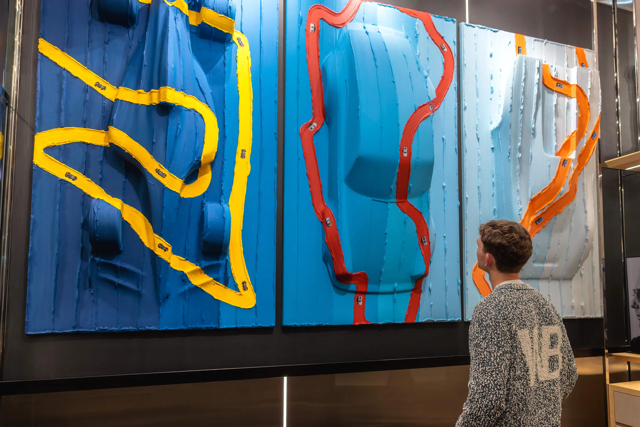 Artist Werner Bronkhorst admires his large-scale triptych installation featuring toy cars and colourful paint tracks on raised panels | EDG Studios