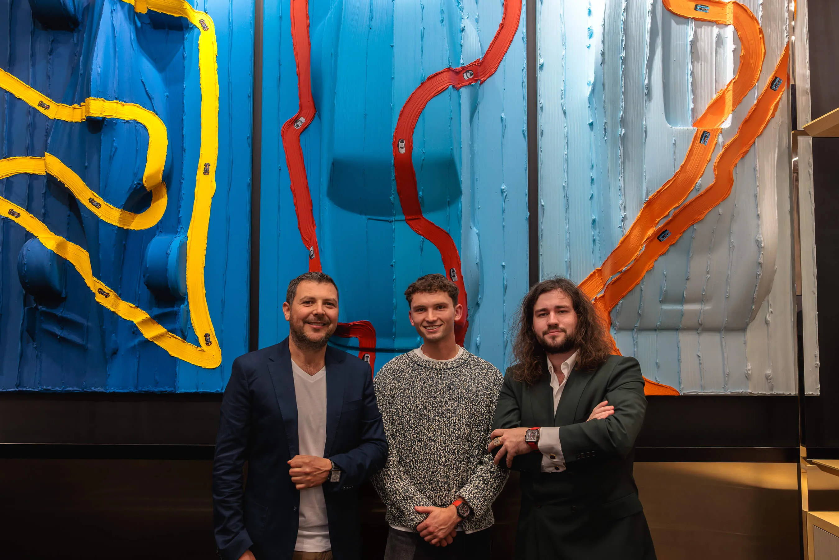 Werner Bronkhorst poses again with two collaborators or guests, smiling in front of the large painted panels in the Tag Heuer store | EDG Studios