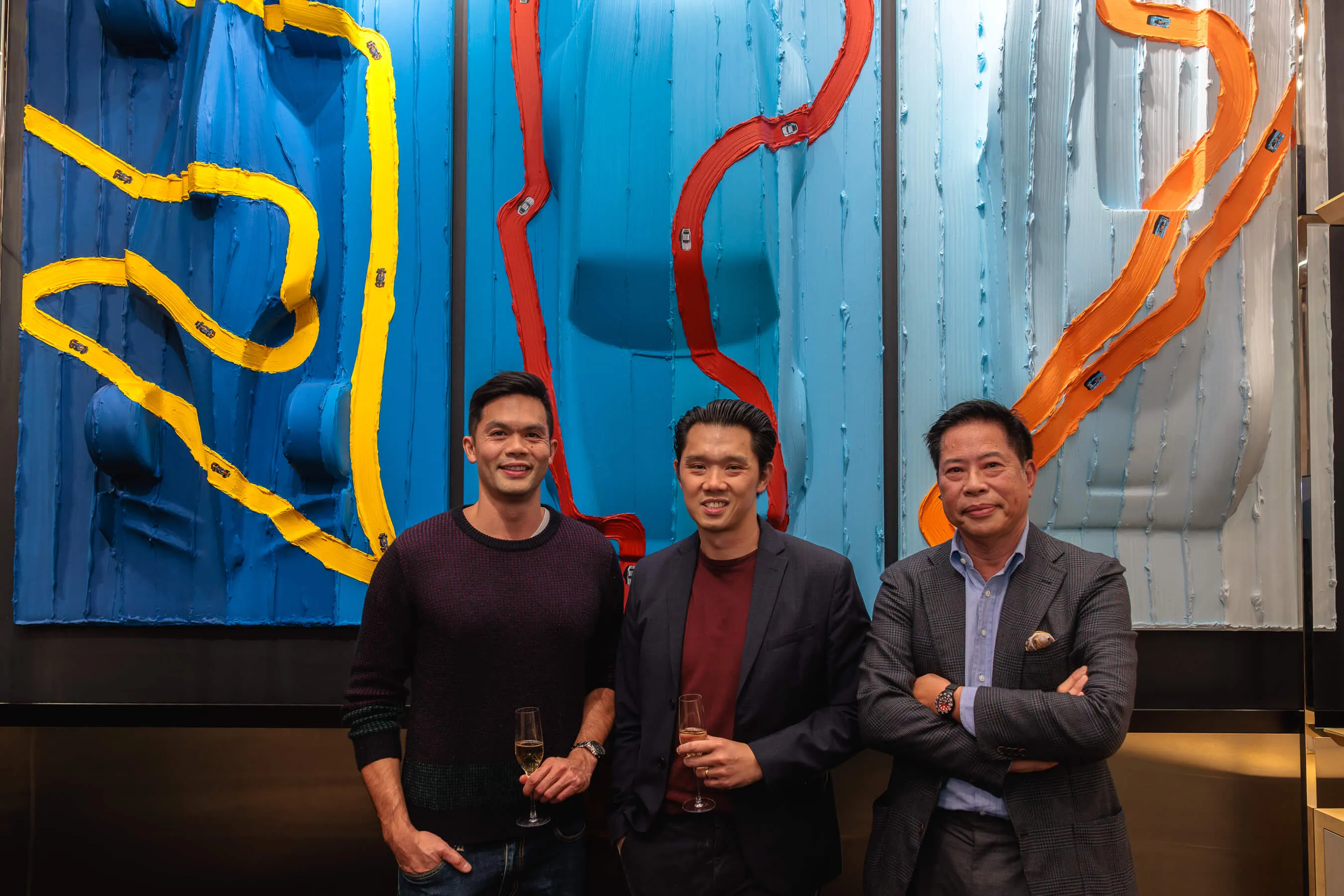 Three guests stand in front of the textured triptych artwork, holding champagne and posing against the brightly coloured panel work | EDG Studios
