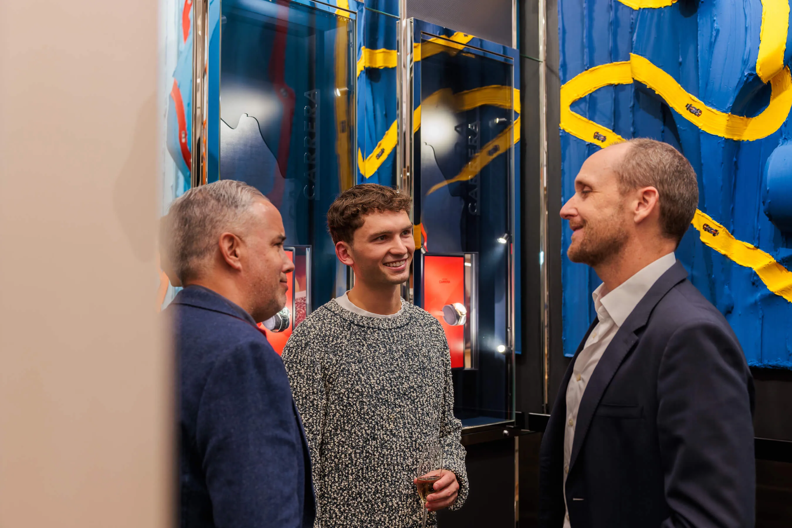 Three men smiling and talking in front of vibrant blue and yellow abstract artwork by Werner Bronkhorst | EDG Studios