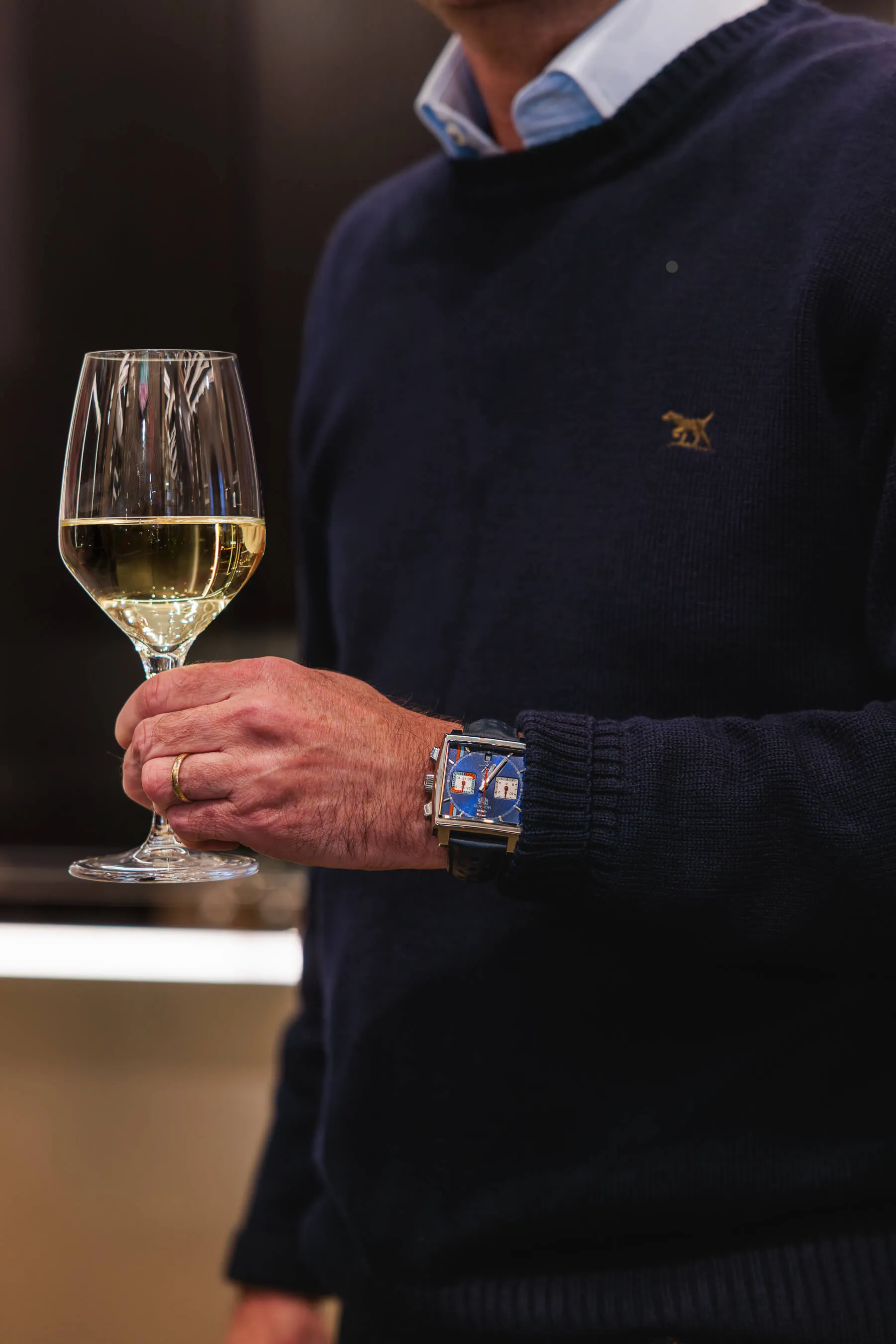 Close-up of a guest wearing a blue TAG Heuer Monaco watch and holding a glass of white wine, showcasing the brand’s signature square dial | EDG Studios