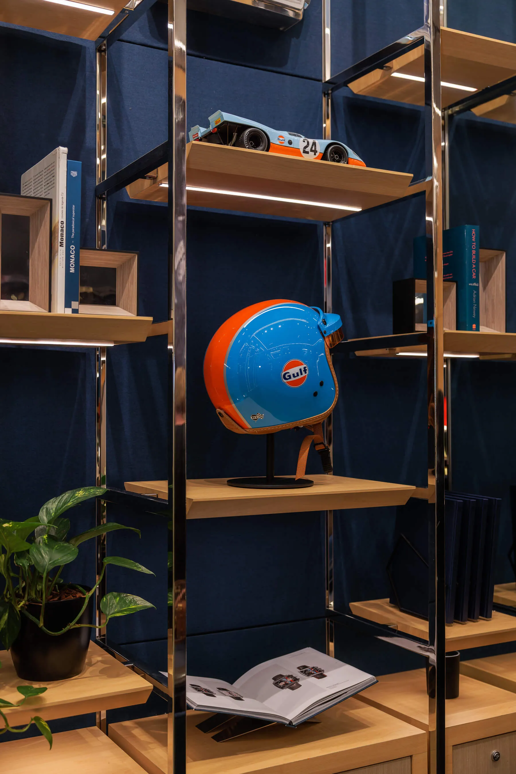 Another angle of the same boutique shelf display, focusing on the retro Gulf helmet and orange-blue model car, with racing books and greenery | EDG Studios