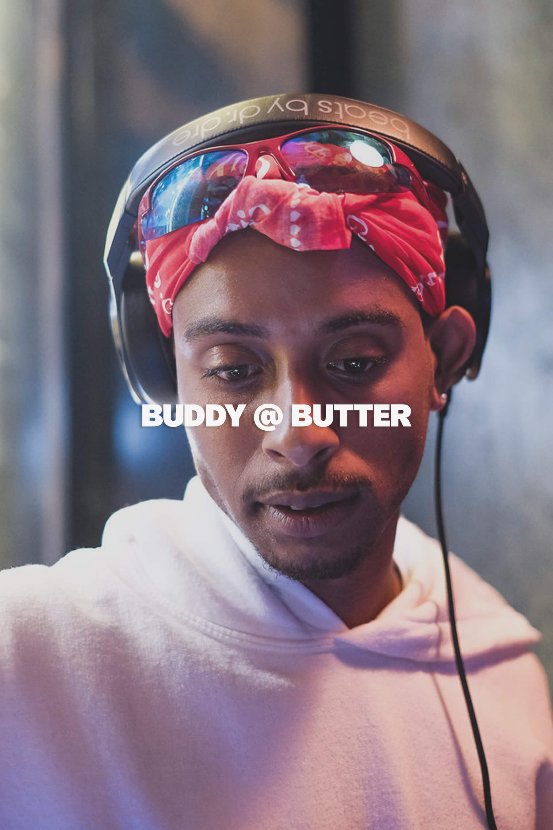Close-up portrait of American rapper and recording artist Buddy wearing Beats headphones and a red bandana with sunglasses on top, DJing at the Butter Sydney restaurant event under moody, colourful lighting.