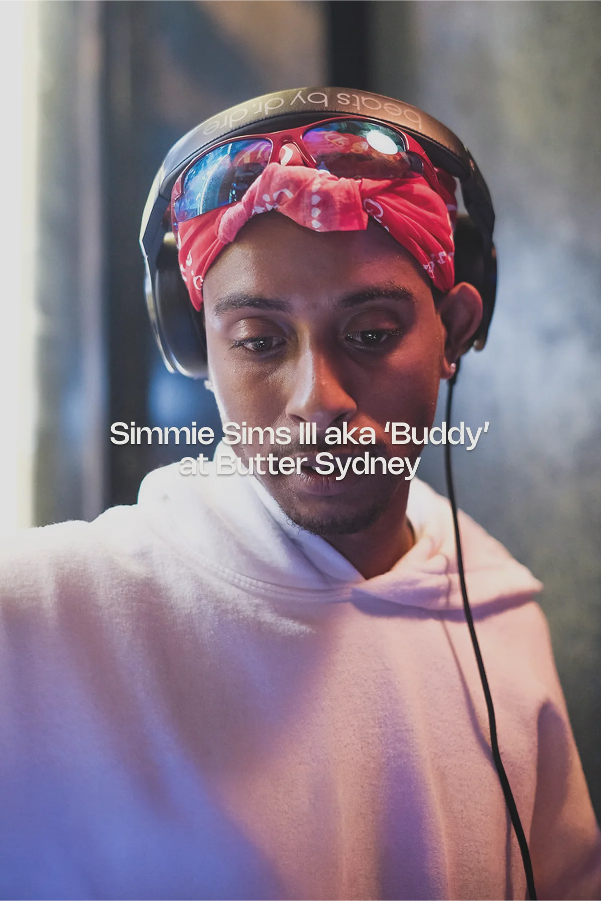 Close-up portrait of American rapper and recording artist Buddy wearing Beats headphones and a red bandana with sunglasses on top, DJing at the Butter Sydney restaurant event under moody, colourful lighting.