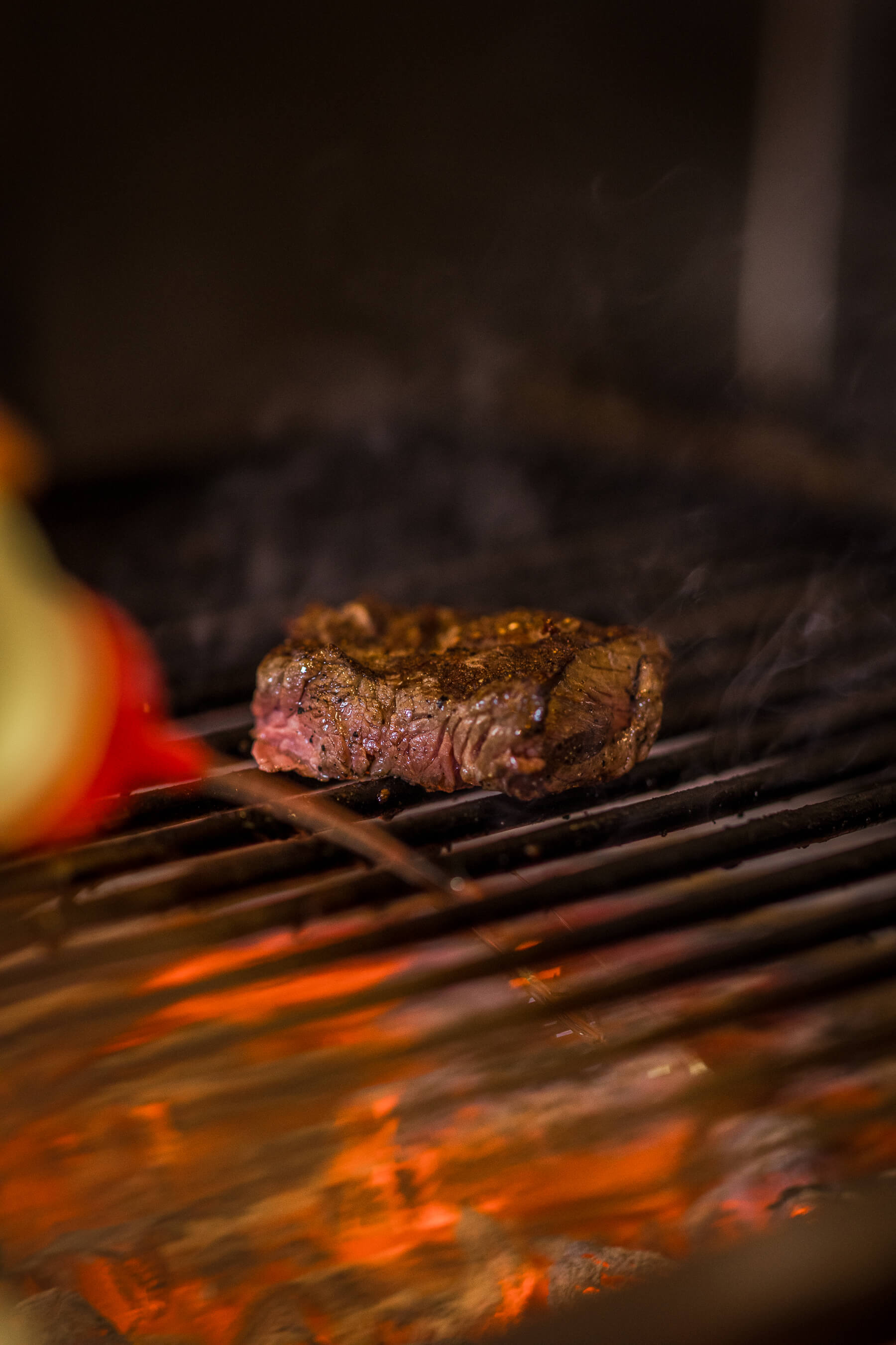 Close-up of a medium-rare steak on the grill at Le Foote, Sydney, with soft smoke and ember glow in the background