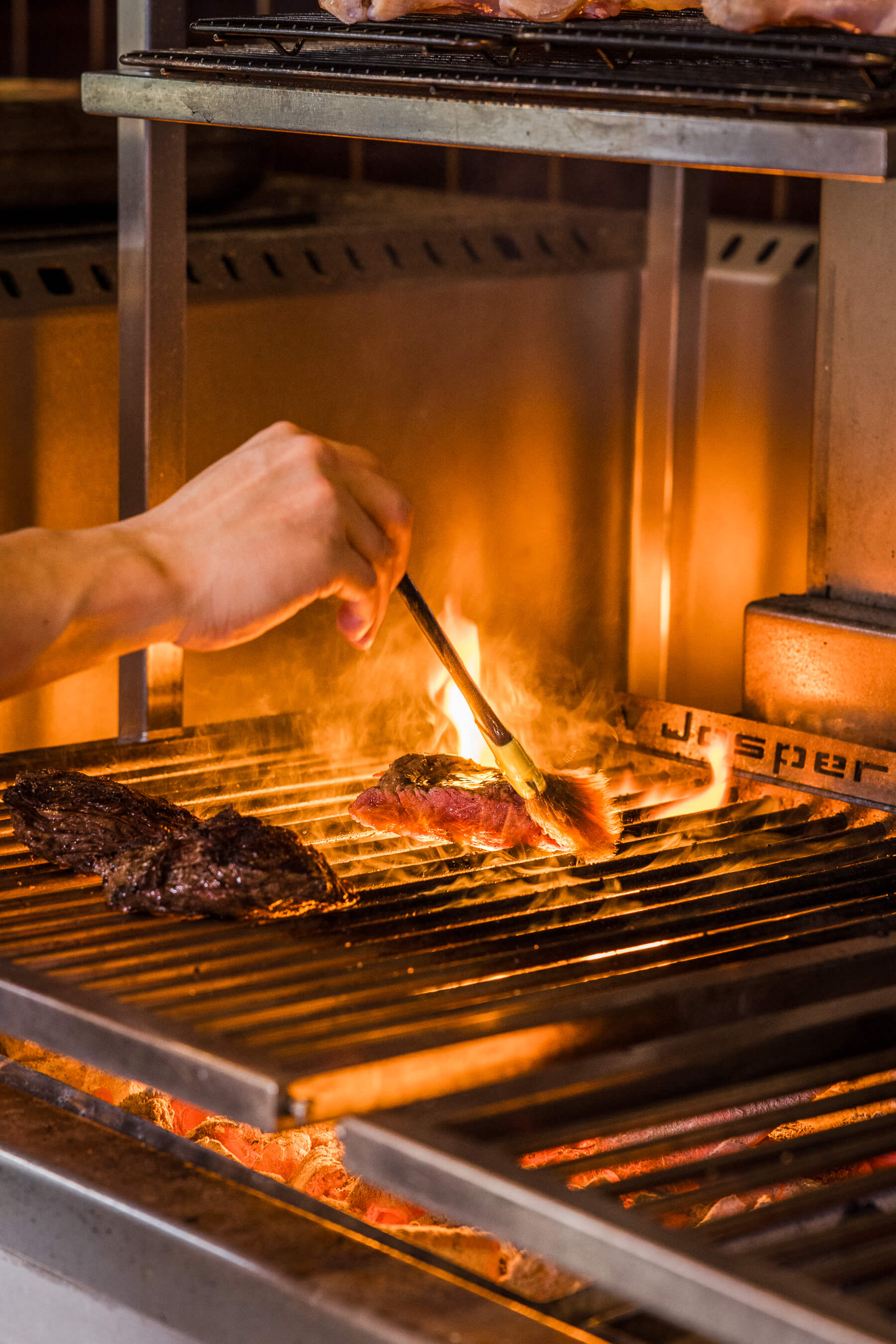 Steak being basted with a brush over an open flame grill at Le Foote restaurant, fire and smoke adding heat and motion