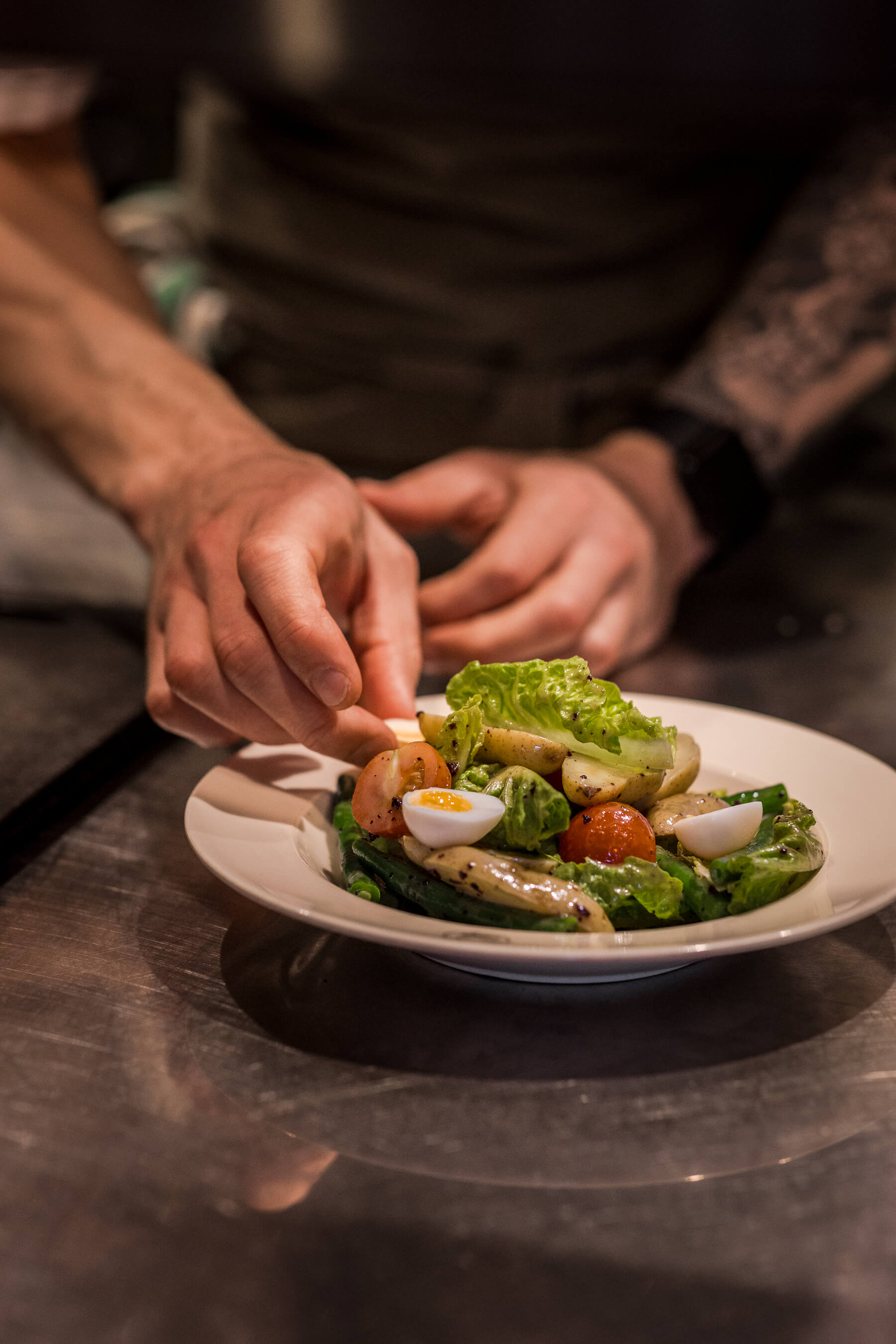 Chef’s hands carefully arranging gourmet salad with cherry tomatoes, lettuce, and quail eggs at Le Foote in Sydney