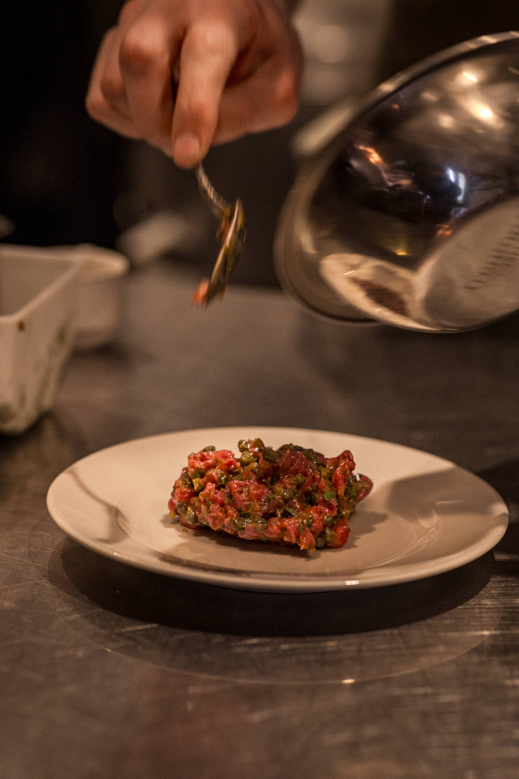 Beef tartare being plated with precision at Le Foote, Sydney, vibrant herbs and rich colour captured mid-service