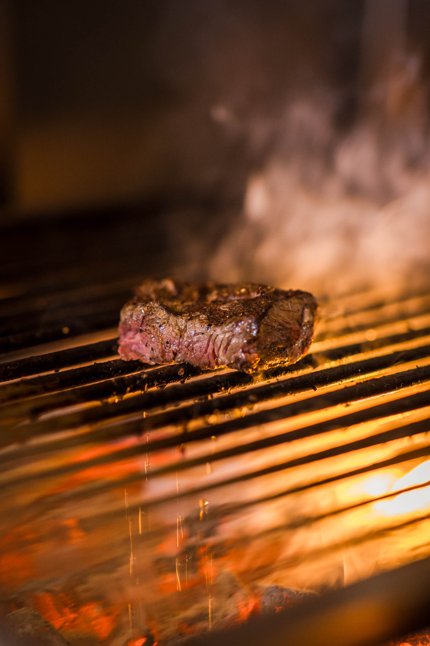 Close-up of juicy steak cooking over open flame at Le Foote restaurant in Sydney, fire and smoke creating a dramatic backdrop