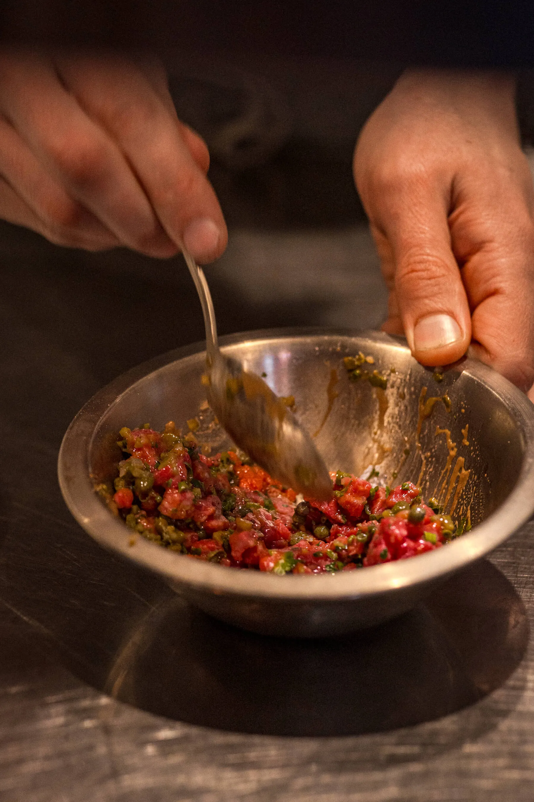 Chef preparing steak tartare in a stainless steel bowl with spoon, finely diced beef and capers at Le Foote restaurant | EDG Studios